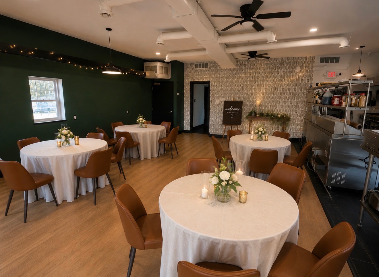 Dining area with round tables, floral centerpieces, and a welcome sign against a deep green accent wall