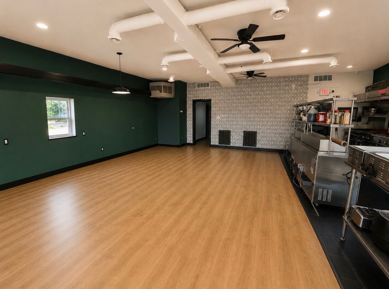 Open event space with hardwood floors, green accent wall, and prep kitchen area