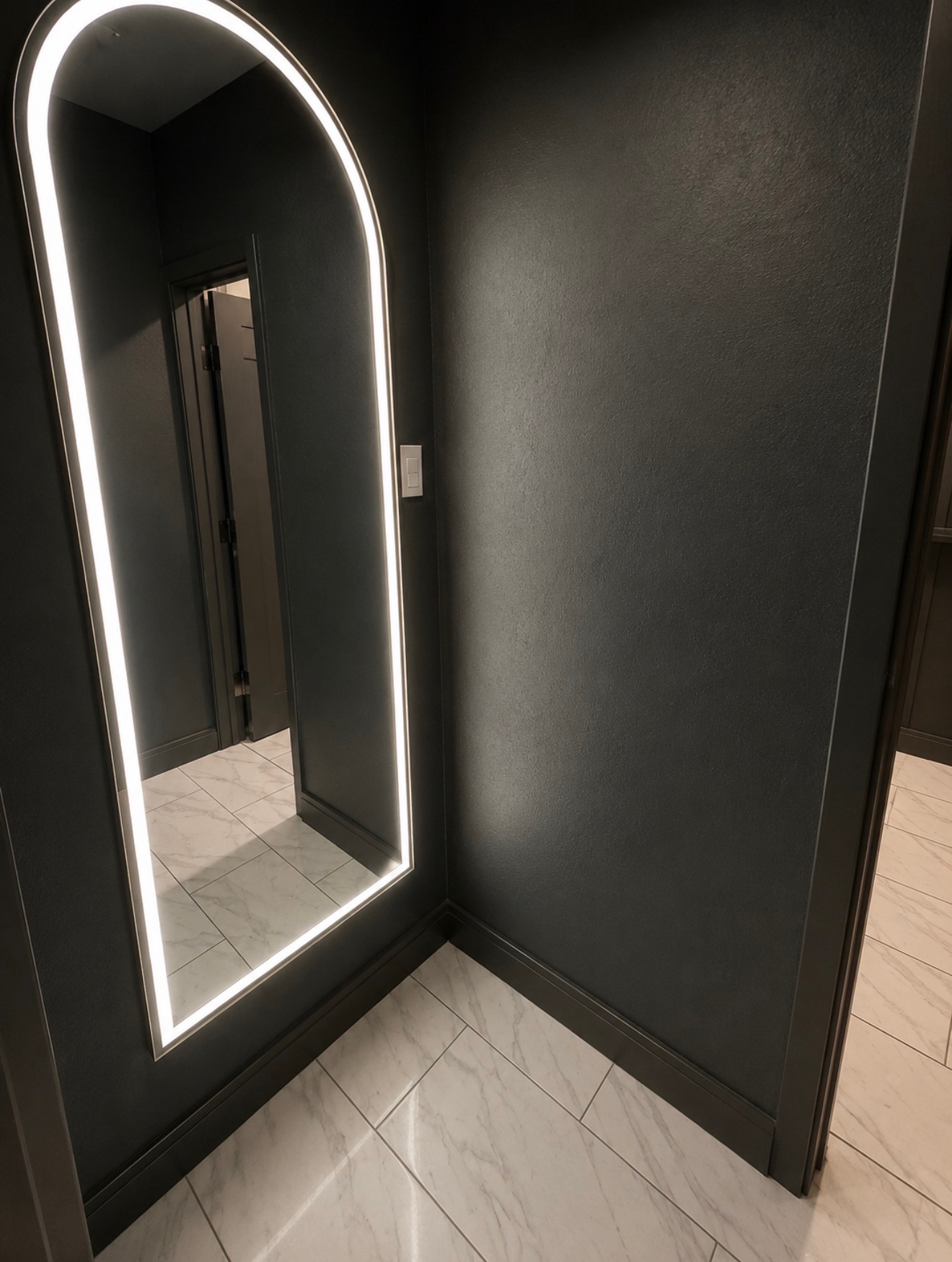Backlit arched vanity mirror in a dark powder room with marble tile flooring