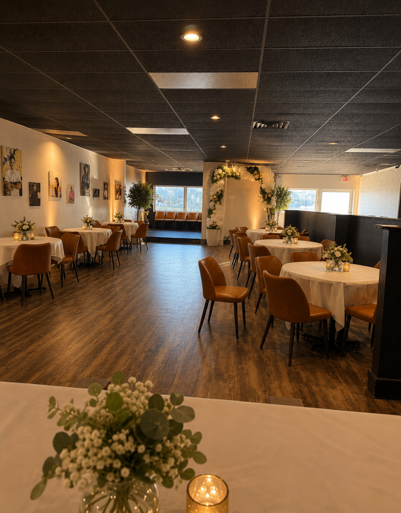 City Light Events main hall styled for a reception with round tables, white linens, tan leather chairs, and a floral balloon arch
