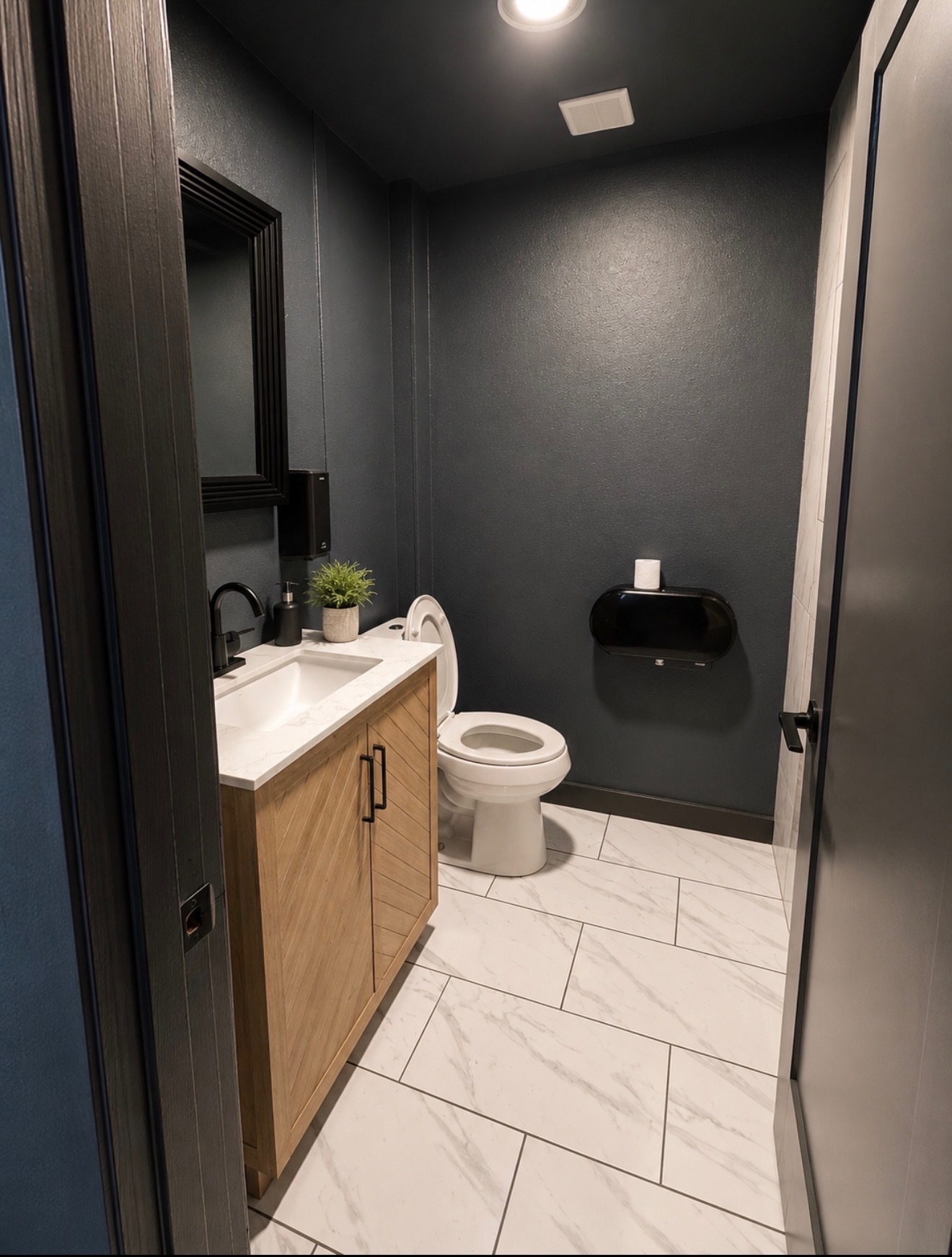 Modern private restroom with dark walls, marble tile, and a wood vanity