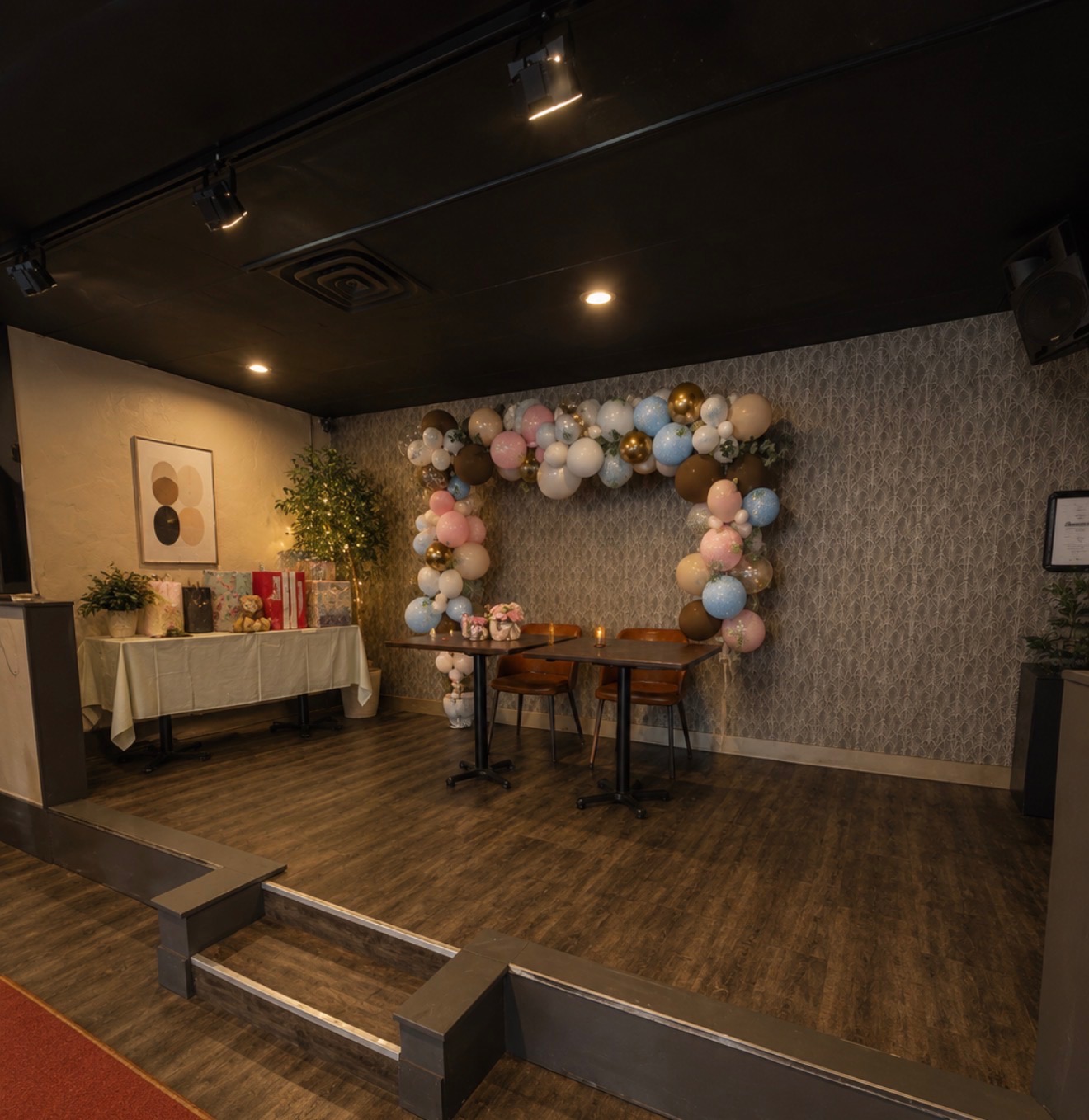Stage area with pastel and gold balloon arch, gift table, and intimate cafe seating